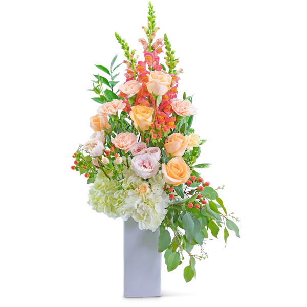Tall floral arrangement with peach roses, pink snapdragons, and white hydrangeas in a white vase