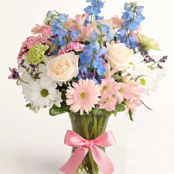 Mixed bouquet of pastel flowers in a glass vase with a pink ribbon
