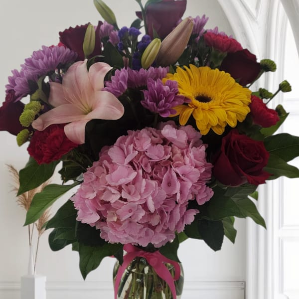 Mixed bouquet of pink, red, purple, and yellow flowers in a glass vase