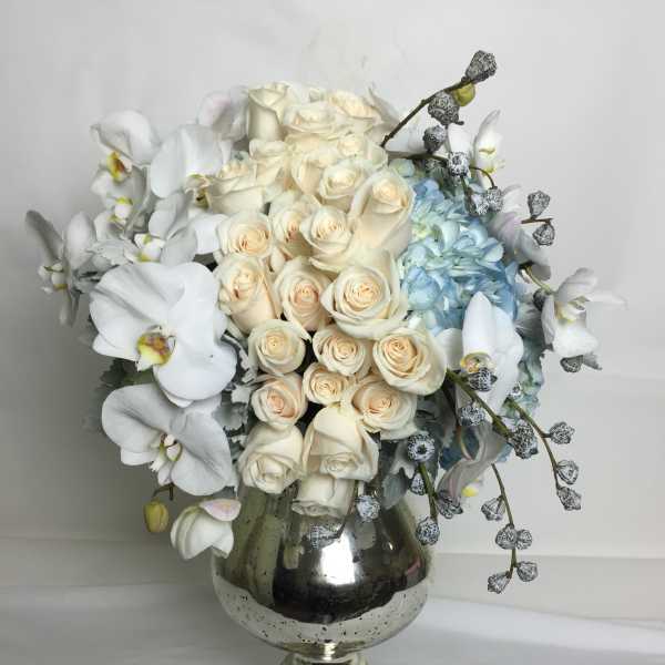 Cream roses and white orchids arranged in a silver vase