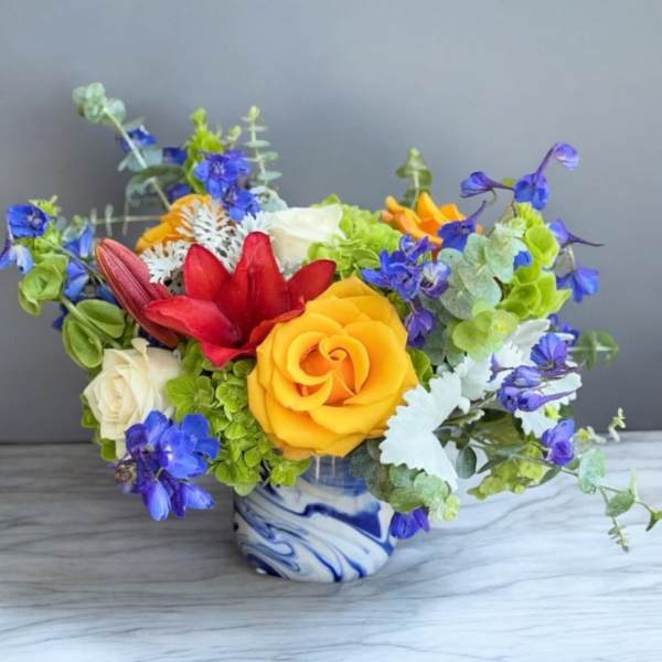Colorful bouquet of roses, lilies, and blue flowers in a blue-and-white vase