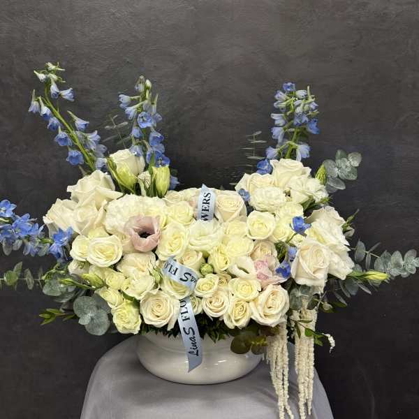 White rose arrangement with blue delphinium in a white vase