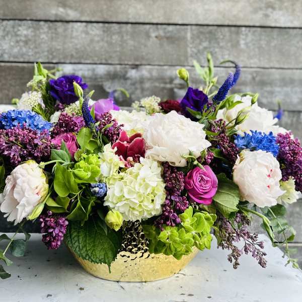 Low floral arrangement in a gold bowl with white, purple, pink, and blue blooms