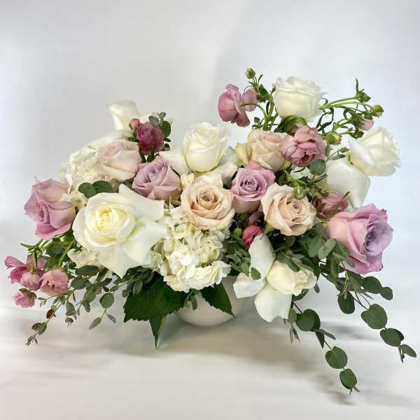 Pastel rose bouquet in a white vase with trailing greenery