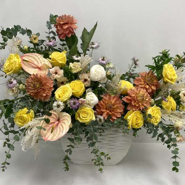 Mixed floral arrangement in a white rectangular vase with yellow and peach blooms