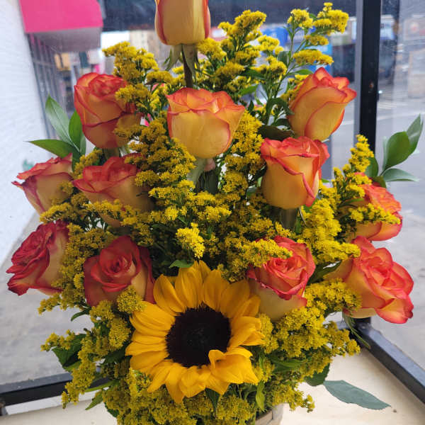 Basket arrangement of orange roses, yellow flowers, and a sunflower