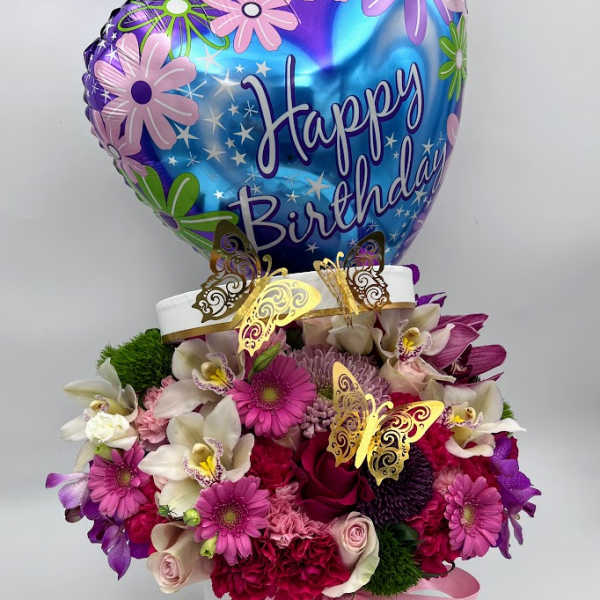 Birthday balloon above a pink and purple flower arrangement in a white box