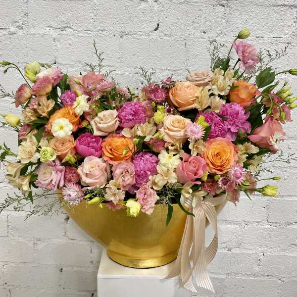 Mixed pink and peach flower arrangement in a gold vase with ribbon
