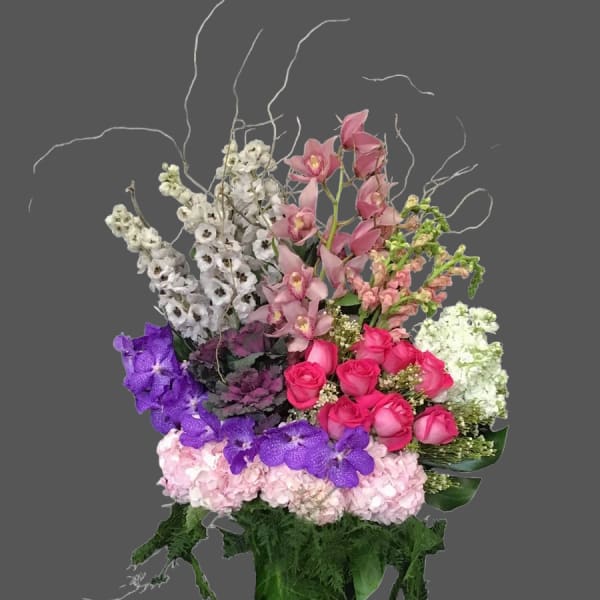 Tall mixed bouquet with pink roses, orchids, and purple flowers in a green vase
