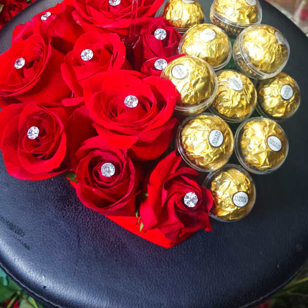 Red roses and gold-wrapped chocolates arranged on a black round box with a card.