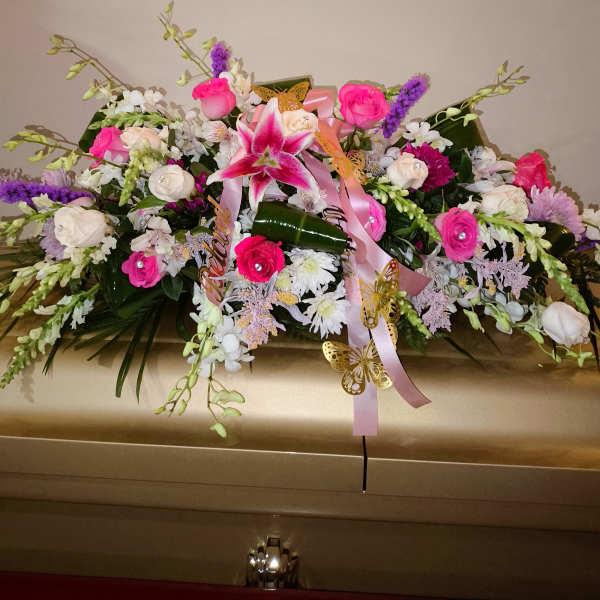 Pink and white floral casket spray with ribbons and butterfly accents