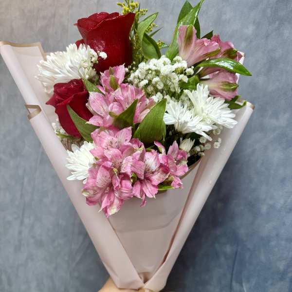 Bouquet of red roses, pink alstroemeria, and white daisies wrapped in blush paper