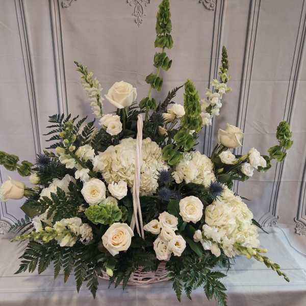 White floral basket arrangement with roses, hydrangeas, and tall green spikes