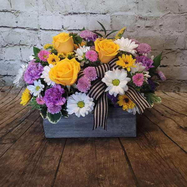 Mixed bouquet of yellow roses, daisies, and purple flowers in a wooden box