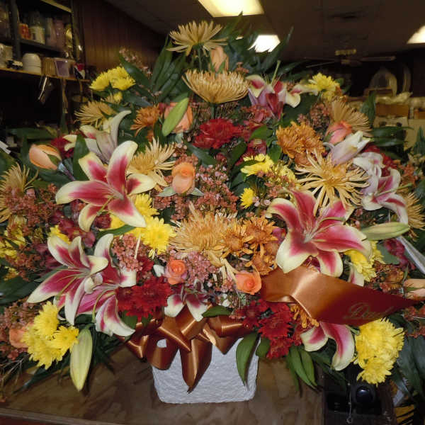 Large mixed floral arrangement with lilies, roses, and chrysanthemums in a white container
