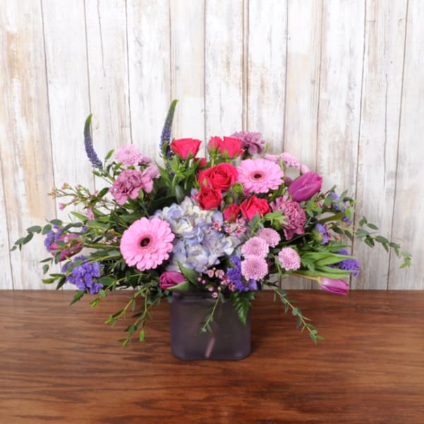 Low pink and purple mixed flower arrangement in a frosted purple glass cube vase
