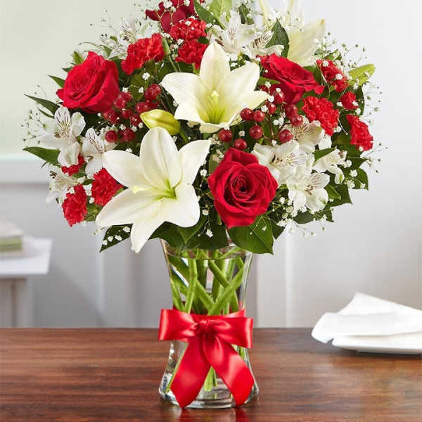 Red roses and white lilies in a glass vase with a red ribbon