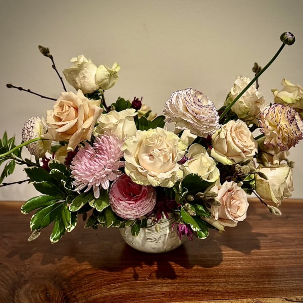 Low arrangement of cream roses, pink mums, and ranunculus in a white ceramic bowl