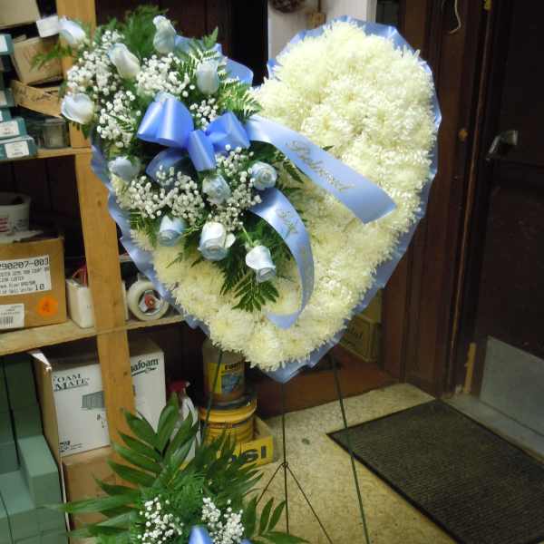 Heart-shaped white floral wreath with blue ribbon and small rose sprays