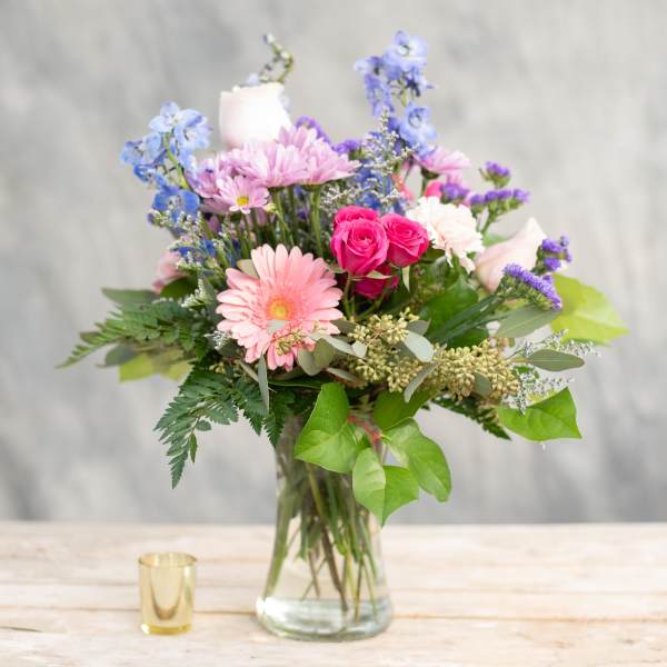Mixed bouquet of pink, purple, and blue flowers in a clear glass vase