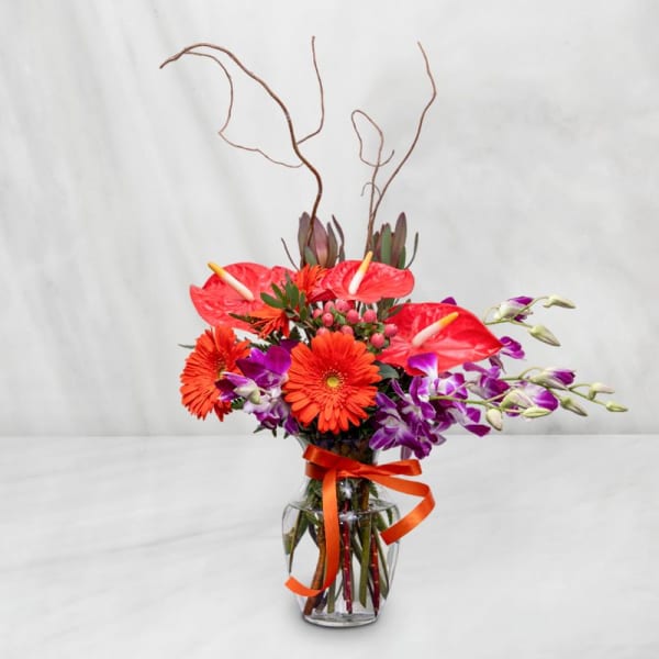Bright mixed bouquet in a glass vase with orange ribbon