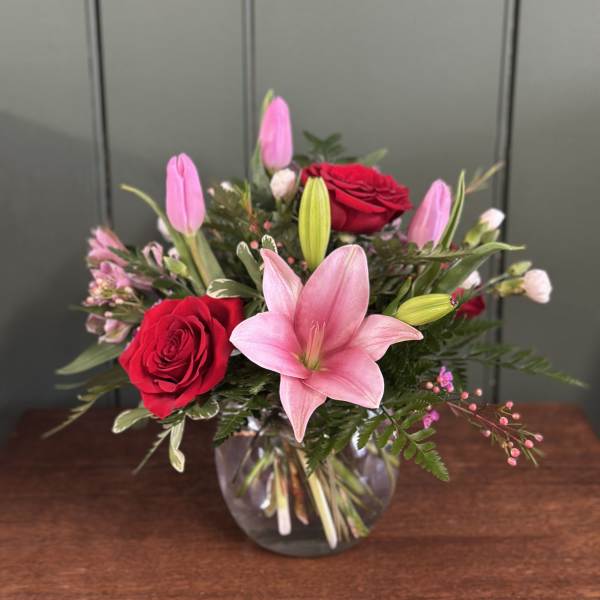 Pink lilies and red roses arranged in a clear glass vase
