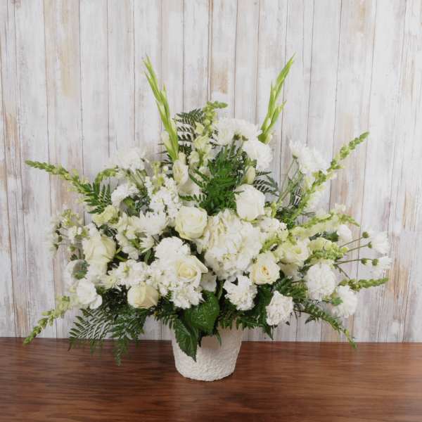 Tall all-white floral arrangement with roses, hydrangeas, carnations, and snapdragons in a white vase