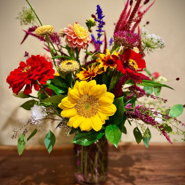 Mixed bouquet with a yellow sunflower and red and pink blooms in a clear glass vase