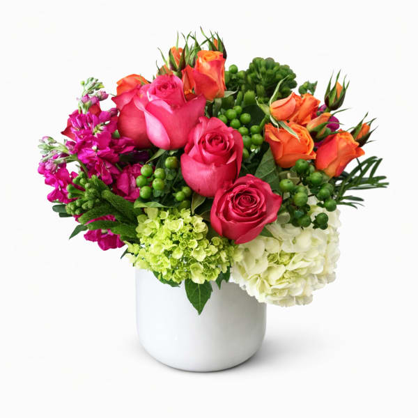 Bright mixed bouquet of roses, hydrangeas, and purple blooms in a white vase
