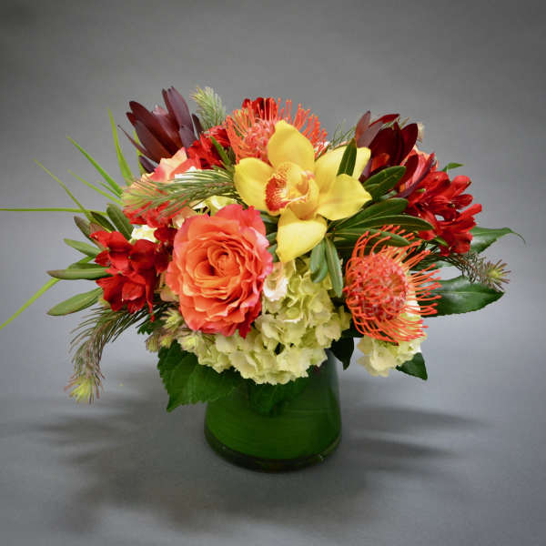Colorful bouquet in a green glass vase with yellow orchids and orange roses