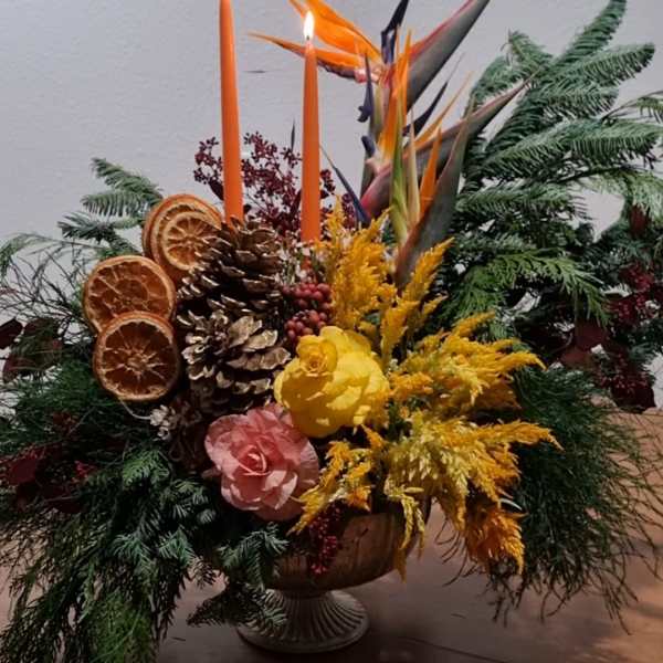 Tropical floral arrangement with orange candles in a pedestal vase