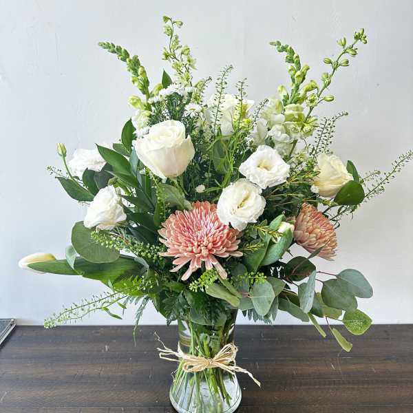 Mixed arrangement of white roses, snapdragons, and peach chrysanthemums in a clear glass vase