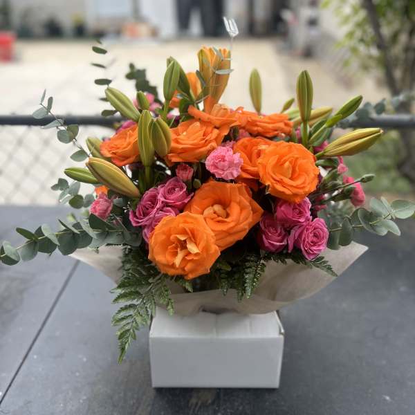 Orange roses and pink spray roses in a wrapped bouquet with lilies