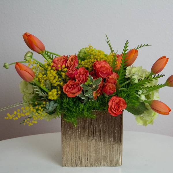 Orange tulips and coral roses in a gold square vase