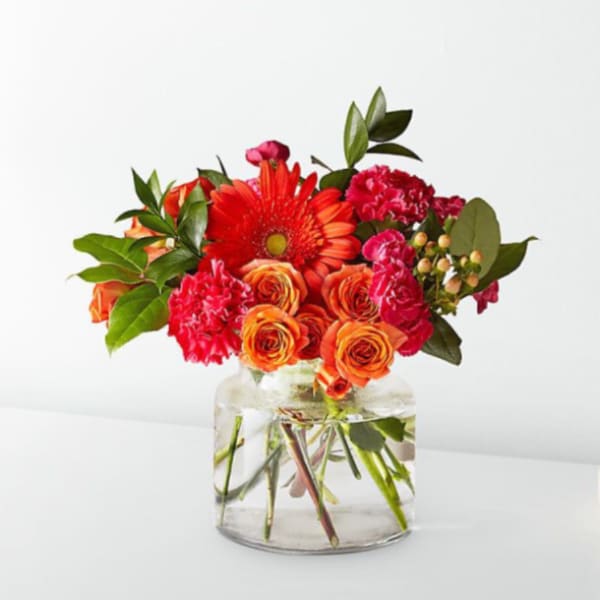 Bright mixed bouquet in a clear glass vase with red, orange, and pink blooms