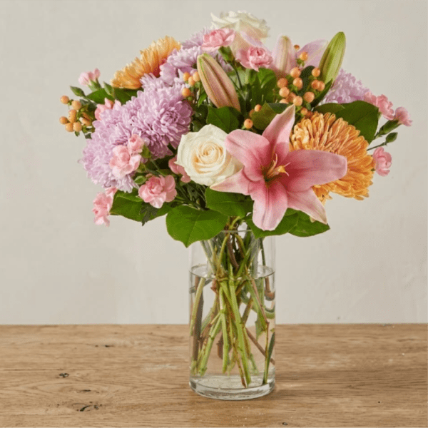 Mixed bouquet of pink lilies, lavender mums, white roses and peach blooms in a clear glass vase