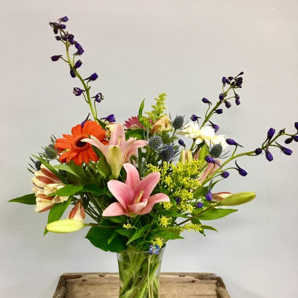 Mixed bouquet of lilies, gerbera daisies, and purple flowers in a glass vase