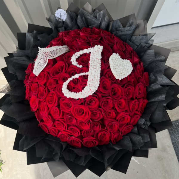 Round bouquet of red roses with white floral initials and a heart on black wrap