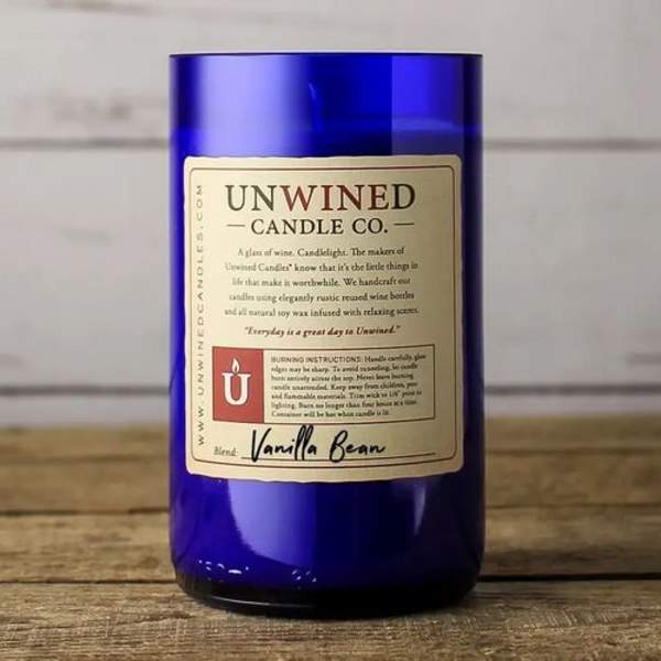 Blue glass jar candle with cream label reading Unwined Candle Co. Vanilla Bean on wooden surface