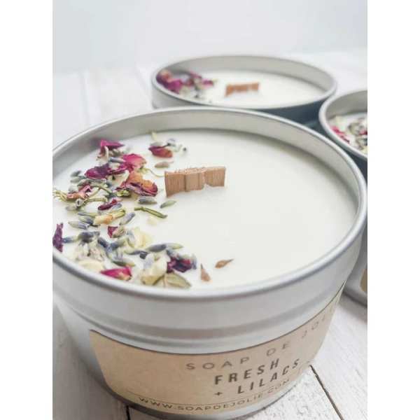 Round tin candles with wooden wicks and dried flower petals scattered on top.