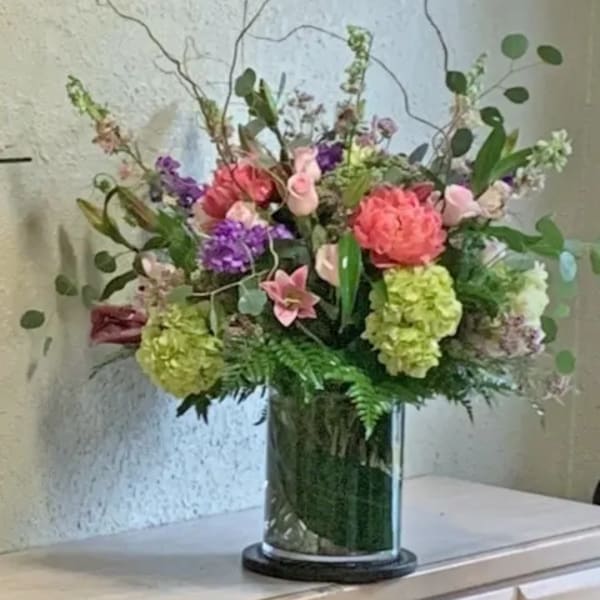 Tall mixed arrangement of pink, green, and purple flowers in a clear glass cylinder vase