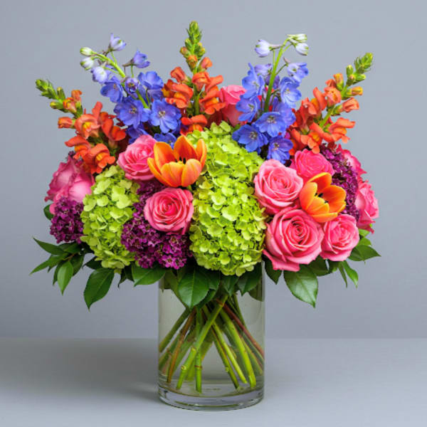 Colorful bouquet of roses, tulips, hydrangeas, and blue flowers in a glass vase
