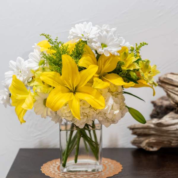 Yellow lilies and white daisies in a clear glass vase