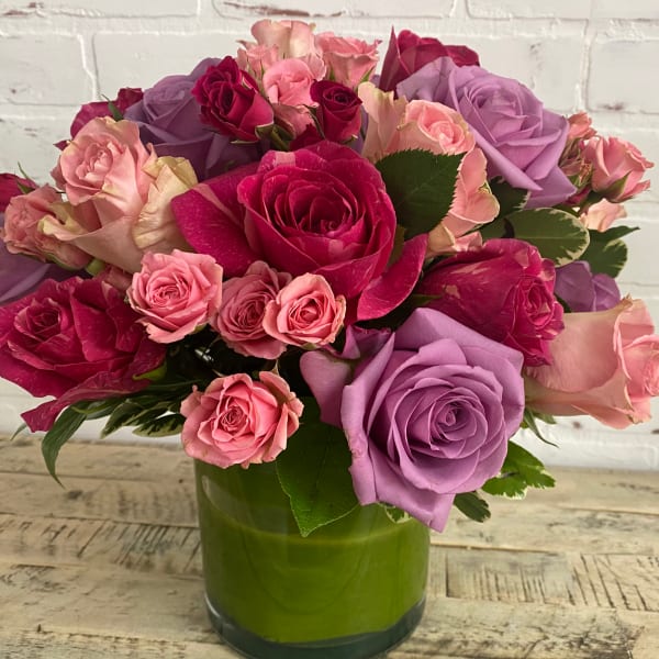 Bouquet of pink, purple, and red roses in a green glass vase