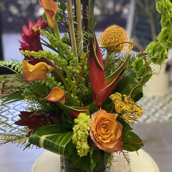 Tropical floral arrangement with orange roses and calla lilies in a glass vase