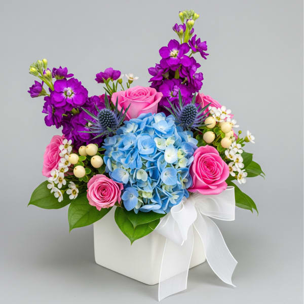 Pink roses and blue hydrangea in a white box with purple flowers