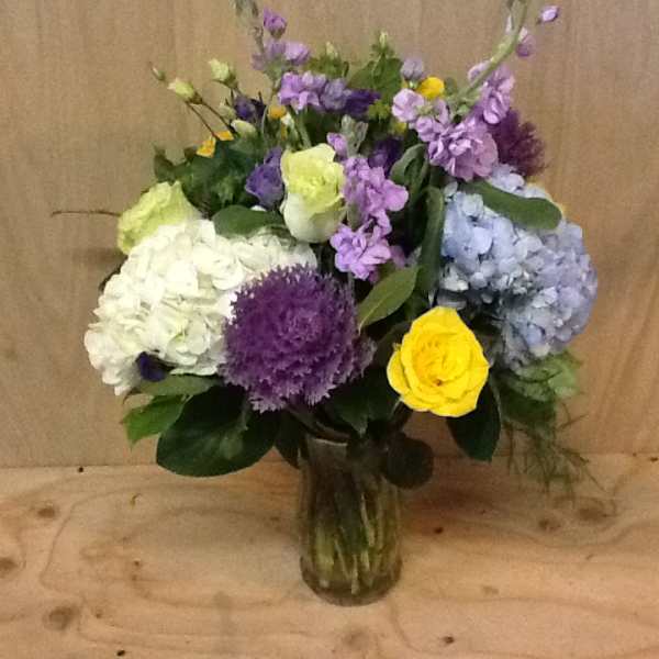 Mixed bouquet of hydrangeas, roses, and purple blooms in a glass vase