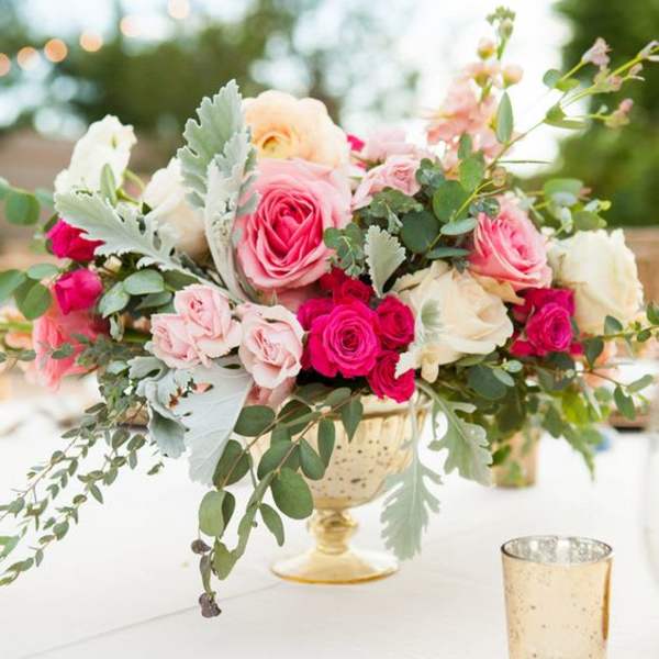 Pink and white roses arranged in a gold pedestal vase on a table