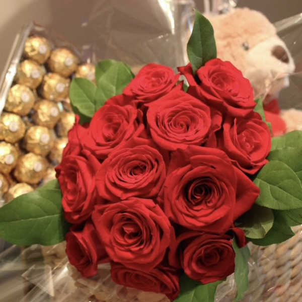 Bouquet of red roses with green leaves beside chocolates and a teddy bear