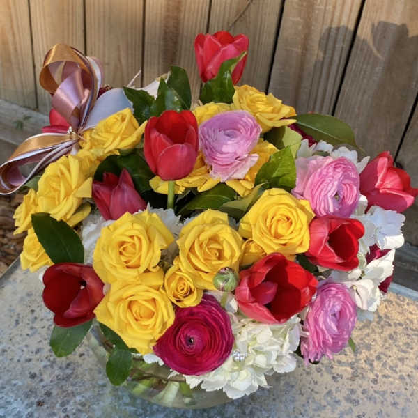 Mixed bouquet of yellow roses, red tulips, and pink ranunculus in a glass vase